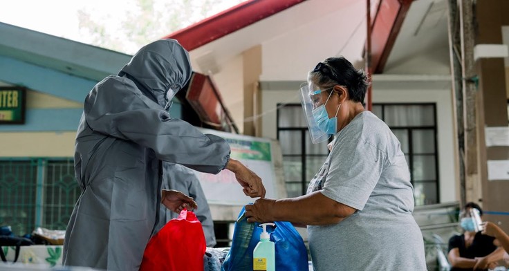 Ein Mensch in Corona-Schutzanzug verteilt Hygieneartikel. 