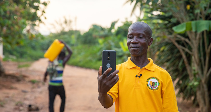 Ein Kakaobauer in gelbem T-Shirt filmt sich mit dem Smartphone.