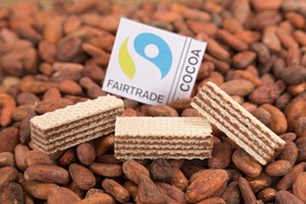 Manner-Waffeln liegen in Kakaobohnen. Das Fairtrade-Rohstoffsiegel ist ebenfalls abgebildet.